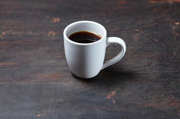 White cup with coffee on a dark wooden background, closeup. Tasty breakfast, morning routine concept