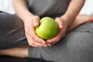 Young woman in grey sweat pants holding green apple for snack. Healthy eating and lifestyle concept. Eat low carbs vitamin fruits for health and weight loss