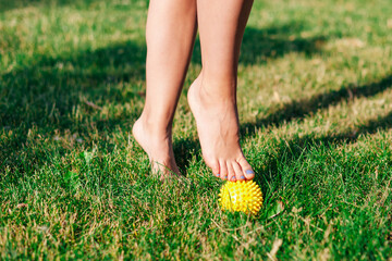 close-up of graceful bare feet of young woman standing on tiptoes on spiked massage ball on green...