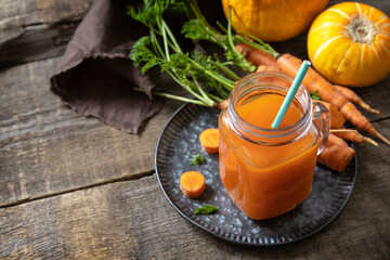 Fresh natural mixed juice, healthy food concept. Glass jar of fresh carrot juice with fresh carrots and pumpkin on a wooden rustic table. Copy space.