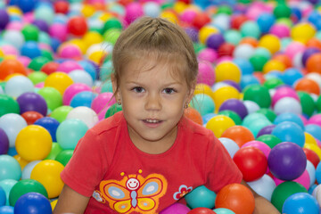 Fototapeta na wymiar Caucasian little girl of five years old looking at camera among multicolor balls in play center