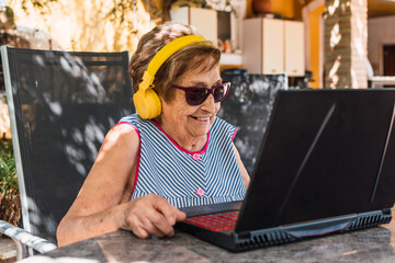 old woman smiling with headphones and sunglasses making a video call outdoors