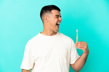 Young handsome man brushing teeth over isolated blue background laughing in lateral position