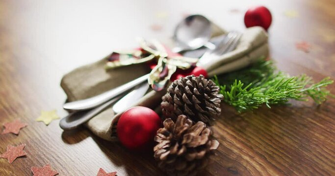 Video of christmas decorations with bauble and pine cones and cutlery on wooden background