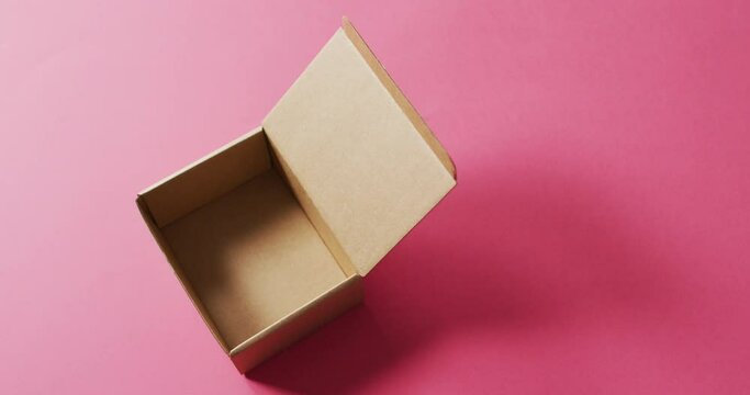 Video of open, empty cardboard box and copy space on pink background