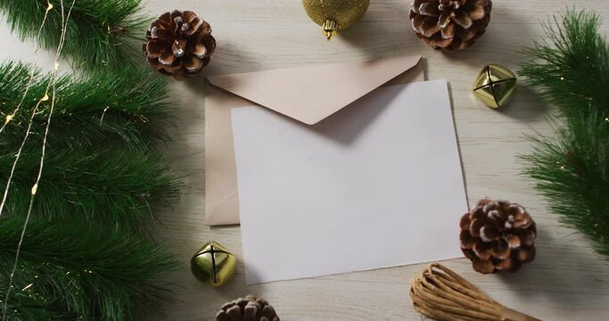 Video of christmas decorations with white card and beige envelope on wooden background