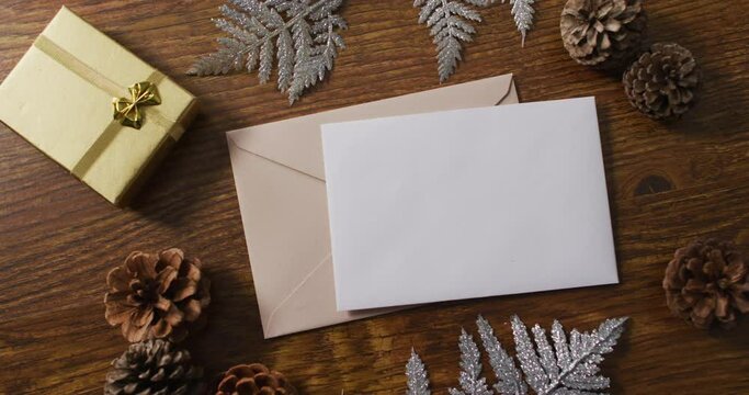 Video of christmas decorations with white card and beige envelope on wooden background