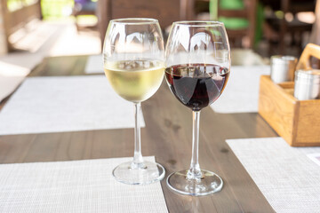 a glass of fragrant white and a glass of ruby red wine on a wooden table in a restaurant, selective focusing, dry white wine in a glass and semi-sweet red, expensive wine