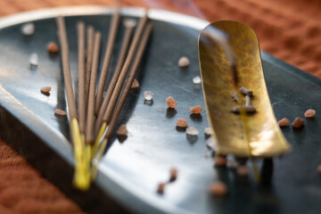 incense sticks laying on a stone tablet and incense burning on the side, orange cloth background.
selective focus, focus on the middle of the incense sticks.