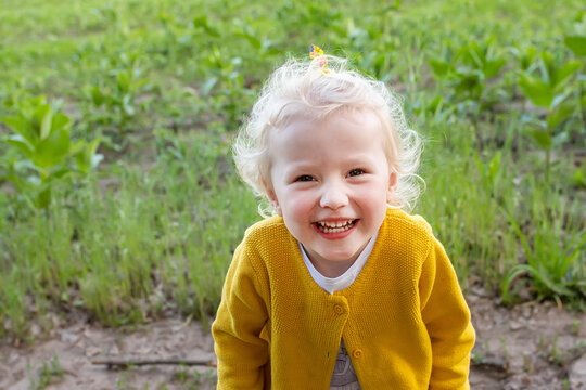 Funny little girl laughs happily. child blonde with smile with all her teeth in background of field. Happy childhood concept.