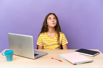 Naklejka premium Little student girl in a workplace with a laptop isolated on purple background and looking up