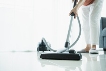 Asian young housekeeper using vacuum machine to clean a dirty floor in the living room. - obrazy, fototapety, plakaty