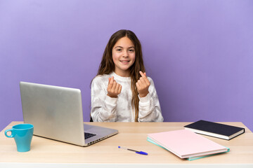 Little student girl in a workplace with a laptop isolated on purple background making money gesture