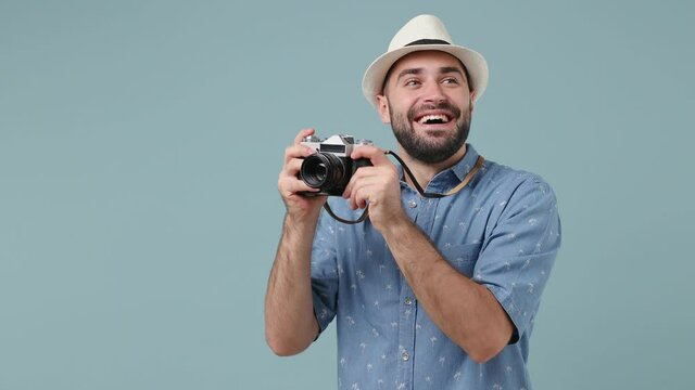 Traveler tourist excited fun young brunet bearded man 20s wears denim shirt straw hat hold retro vintage photo camera taking pictures isolated on pastel light blue background. Passenger travel abroad