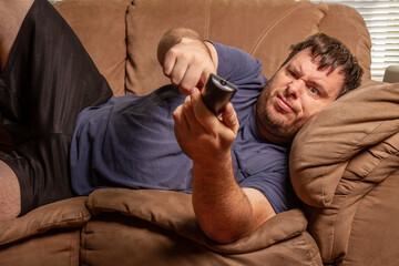 Fototapeta premium confused man trying to push buttons on the remote for the tv