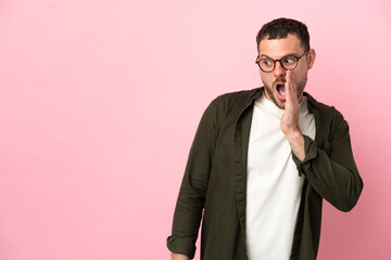 Young Brazilian man isolated on pink background whispering something with surprise gesture while looking to the side