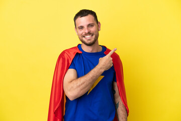 Super Hero Brazilian man isolated on yellow background pointing to the side to present a product