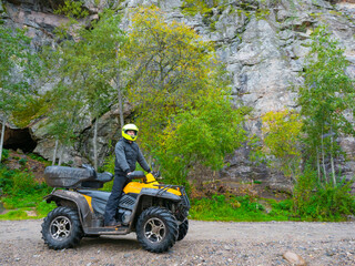 A man on an ATV on a rock background. The quad bike driver looks into the distance. Travel by ATV....