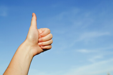 A human hand against the background of a blue sky shows a gesture denoting the class, is demonstrated by showing the thumb up, the rest are folded to the palm, copying the space.