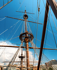 Fototapeta premium The masts of a large sailing ship without sails against the blue sky, with houses visible in the background. The ship is moored. Background with a sailboat.