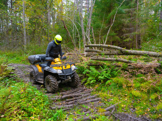 Man in a yellow helmet on an ATV. He rides his ATV through the forest. Off-road driving concept. ATV driver overcomes an obstacle on the road. Quad bike as a symbol of motorcycle racing © Grispb