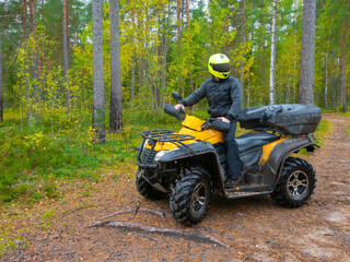 Fototapeta na wymiar ATV racing concept. The ATV driver has stopped and looks around. Quad bike as a symbol of extreme sports Traveling through the forest on a quad bike. Man rides his own ATV. Extreme atv racing