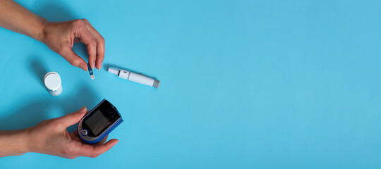 woman measures blood sugar with a glucometer.Diabetes concept on blue background. Banner