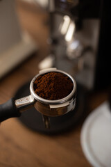 Tool for preparing professional espresso coffee against the background of a wooden table and a coffee grinder. Holder with ground coffee inside.