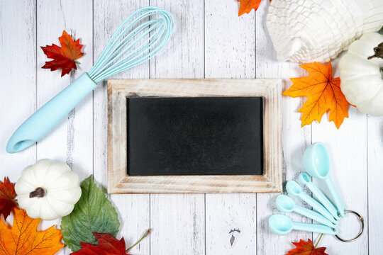 Baking theme chalkboard sign mockup. Thanksgiving farmhouse theme with turkey, white pumpkins and autumn fall leaves, on a white wood background. Negative copy space.