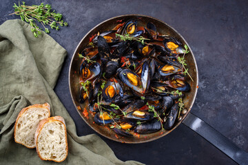 Traditional barbecue Italian blue mussel in tomato red wine sauce with baguette bread as top view in a rustic iron pan