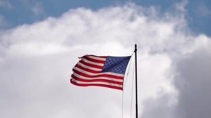 A tattered or weathered American Flag with red and white stripes and 50 stars flaps in the wind with a damaged ragged edge as a symbol of freedom in the United States of America.