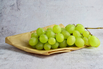 Bunch of grapes in a small kraft paper bag. Stone background, copy space.