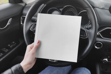 Square book in the girl's hand on car steering wheel mockup