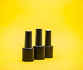 three black bottles of gel nail polish on a yellow background, advertising nail polish