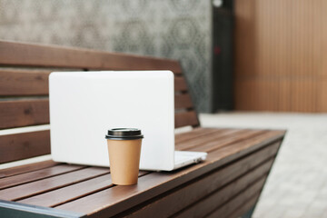 laptop and paper cup of coffee on wooden bench