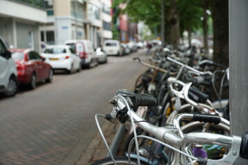 Parked bicycles along the street in Rotterdam, Netherlands. There are parked cars on the other side of the street there are parked cars. Photo taken with selective focus.