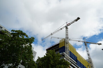 Corporate building in construction with two cranes around it. Building is covered with protection net in yellow and blue colors. Low angle view with copy space. Scene from Rotterdam in Netherlands.