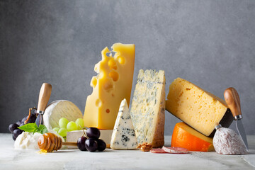Different types of cheese. Cheeses mix maasdam, cheddar, dor blue, camembert, brie and grapes, walnuts, honey on light grey table and background.