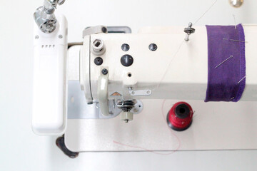 Industrial sewing machine, top view. There is a lamp on the side. There is a spool of thread on the table.