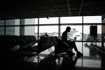 A man wearing face mask while sitting at airport airplane. New normal traveling during a pandemic. Male passenger traveling. Wearing mask in aircraft cabin. Travel Covid-19 Work from plane on laptop