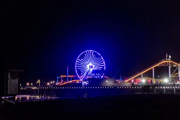 Gardinen The lights of the Santa Monica Pier, the Ferris wheel and the Rollercoaster reflected in the water of the Pacific Ocean on Santa Monica Beach. © John McAdorey