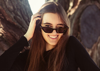 Beautiful toothy laughing winking woman looking happy in fashion sunglasses outdoors summer green...