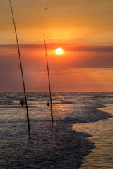 Fishing rod with fishing reel on the beach on a beautiful sunset. Vertical photo