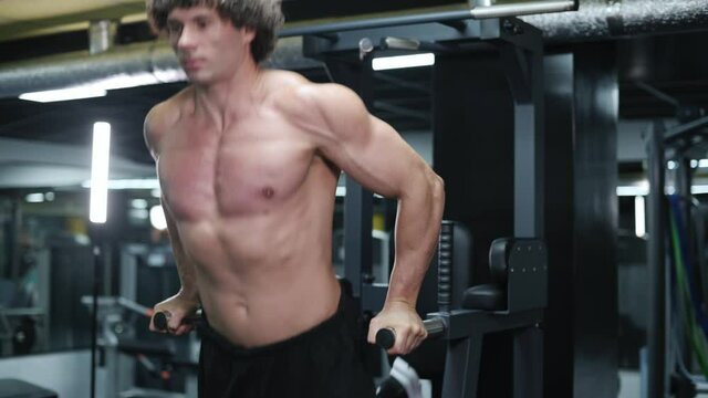 Man exercising on parallel bars. Young athlete exercising in gym. Steadicam shot.
