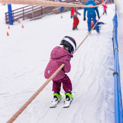 Fototapeta na wymiar Ski training slope. Young child on ski going up on slope with surface baby lift