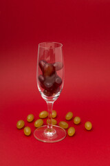 Twelve grapes in glass for sparkling wine cava. Spanish traditional to eat twelve 12 berries for good luck at midnight. Christmas New Year composition. Selective focus, red background, copy space