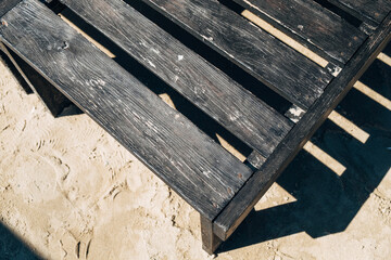 Part of a dark wooden deck chair on the sand.