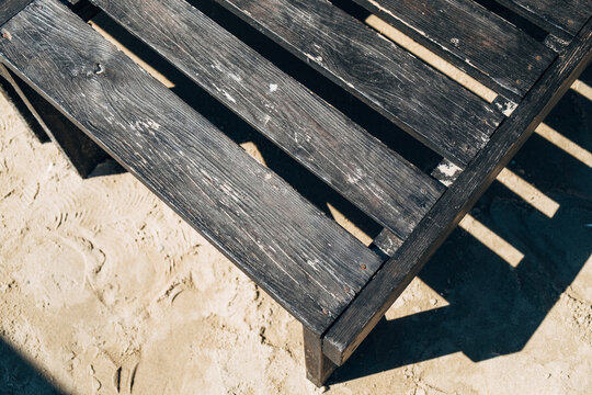 Part Of A Dark Wooden Deck Chair On The Sand.