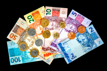 Obraz na płótnie Canvas Current money in Brazil in the year 2020. Notes of 100, 50, 20, 10 and 5 reais and coins of 1.0 reais and 50,25,10 and 5 cents. Back of banknote with its animal symbol.Top view on black background