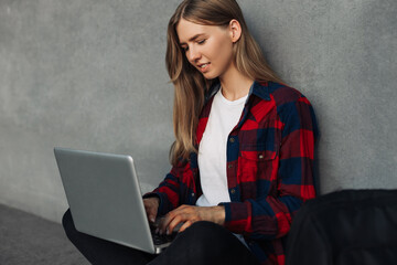 Happy young woman with backpack, in casual clothes, sitting on the floor with crossed legs and...